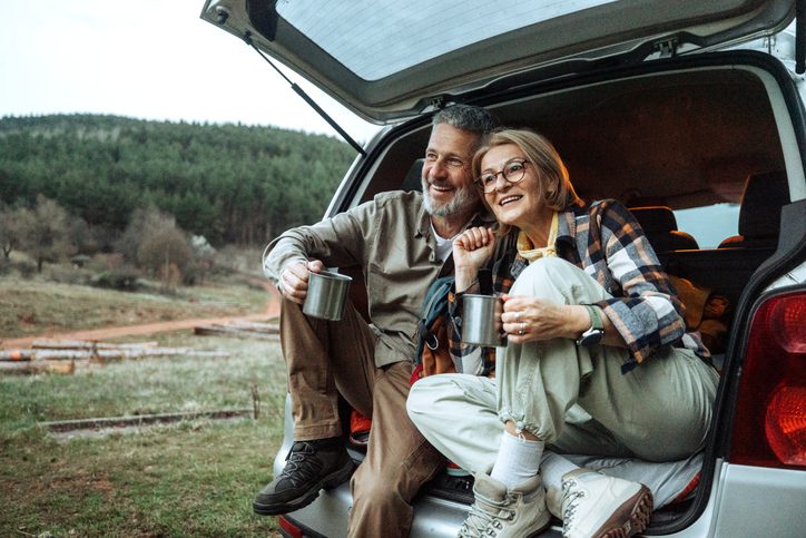 Happy mature couple drinking coffee at car trunk in wilderness